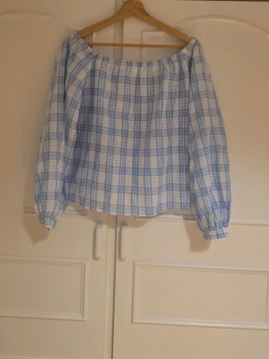 Blåvit offshoulder blus i rutigt - Snygg offshoulder blus i blåvitt rutigt mönster. Blusen har långa ärmar med resår vid ärmslut och en lös, luftig passform.