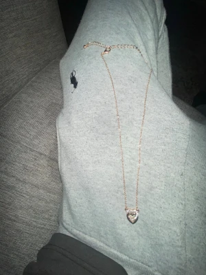 Halsband med hjärthänge i guldton - Snyggt halsband i guldton med ett hjärthänge dekorerat med små pärlor runt kanten. Kedjan är tunn och elegant, perfekt för att ge en söt touch till din outfit. Hjärtat har en glittrig look tack vare pärldetaljerna. Det är rosé guld 