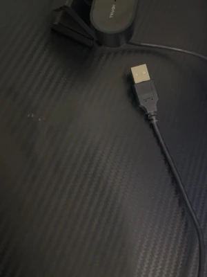 Svart webbkamera från Trust - Säljer en svart 1080p webbkamera från Trust med USB-anslutning. Kameran har en kompakt och rundad design med ett justerbart fäste som gör den enkel att placera på skärmen. Tillverkad i plast och passar perfekt för videosamtal och streaming.