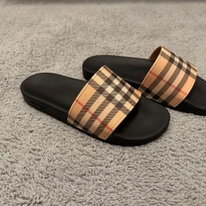 Sandaler med rutigt mönster  - Snygga sandaler med klassiskt beige, svart och rött rutmönster på remmen. Sulan är svart och har en stilren design. Perfekta för en trendig och avslappnad look. sulan är utformad av foten för extra komfort. Storlek 44 men passar som 43! Aldrig använda!