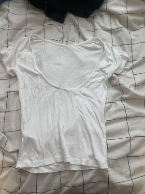 Vit croppad t-shirt med djup urringning - Vit croppad t-shirt med korta ärmar och djup rund urringning framtill. Enkel och stilren design som passar perfekt till jeans eller kjol. Tillverkad i mjuk bomull för en skön känsla hela dagen.