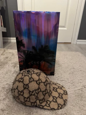 Beige ullkeps från Gucci - Säljer en beige keps från Gucci i ullmaterial med det klassiska GG-monogrammet i svart över hela kepsen (strl M). Köpt hos FLANNELS 2020 och knappt använt då jag inte ville förstöra den. Väldigt sällsynt keps i mycket fint skick skulle nästan säga att den känns helt ny. Hittar tyvärr inte det fysiska kvittot kan leta noga om så önskas vid köp annars kan jag visa dom digitala kvittorna privat då jag nt vill ha namn och adress här ute :)