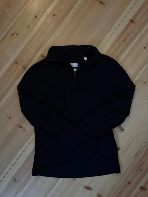 Mörkblå merinotröja från These Glory Days - Säljer en mörkblå långärmad tröja från These Glory Days i mjuk merinoull. Tröjan har halv dragkedja framtill och hög krage, perfekt för lager på lager. Enkel och stilren design som passar till det mesta.