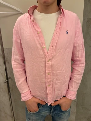 Rosa linneskjorta från Ralph Lauren - En lite schysstare ljusrosa skjorta i linne från Ralph Lauren med klassisk button-down krage och blå broderad logga på bröstet. Skjortan är i bra skicka och är i storlek 14-16 som motsvarar XS. Hör av er vid frågor!🙌