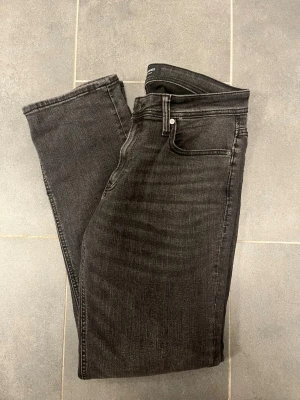 Jack&jones jeans regular Clark  - Säljer ett par svarta regular jeans från Jack&jones . Jeansen har klassisk femficksdesign, diskret broderad bakficka och mär tillverkade i stretchigt denimtyg för extra komfort. Perfekta för en clean och stilren look.