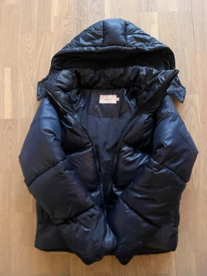 mörkblå pufferjacka från Nelly - Snygg mörkblå pufferjacka från Nelly med stor huva och dragkedja framtill. Jättefin jacka som även håller värmen. Aldrig använd men lappen är avdragen då jag trodde att jag skulle behålla den. Alltså inga defekter på den. nypris:799. slutsåld i alla storlekar 