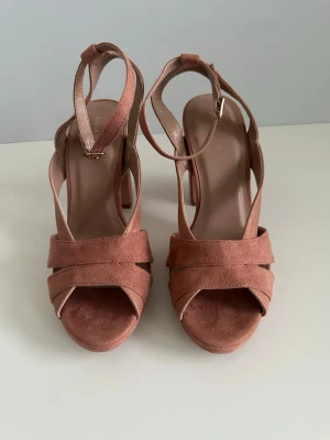 Puderrosa Anna Field sandaler, 40 - Superfina helt NYA högklackade skor / sandaler från Anna Field i storlek 40.  Bekväm bred klack och korsade remmar framtill. Färgen är dammigt rosa i kvalitativ mocka-imitation . Justerbar ankelrem med spänne för perfekt passform. Lika snygga till byxor som till kjol. 