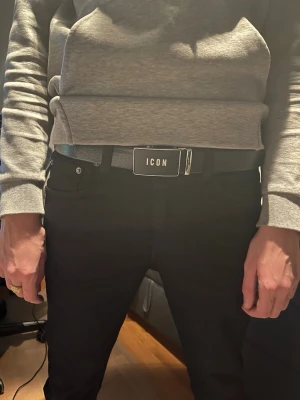 Dsquared icon bälte - Snyggt svart bälte från ICON med ett stilrent metallspänne där det står 'ICON' i vitt. Bältet är gjort i präglat skinn och har en modern, clean look som passar till jeans eller byxor. Perfekt accessoar för att lyfta din outfit.