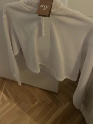 Vit cropped hoodie från Aim'n - Snygg vit cropped hoodie från Aim'n med broderad logga på bröstet. Hoodien har huva med dragsko och långa ärmar. Perfekt för en avslappnad och trendig look. Mjuk och skön bomullsblandning.