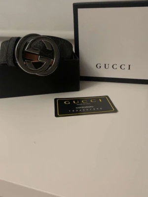 Svart Gucci bälte med GG-spänne - Snyggt svart bälte från Gucci med det klassiska GG-spännet i silverfärg. Bältet har diskret mönster på remmen och känns riktigt lyxigt. Perfekt accessoar för att lyfta vilken outfit som helst.