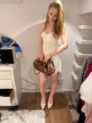 Vit kort klänning  - Söt vit kort klänning med sweetheart neckline, axelbandslös. Klänningen har markerad midja med pärlor i olika mönster och lätt utställd kjol, perfekt för sommarens varma dagar. 