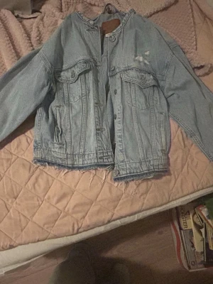 Ljusblå Levi's jeansjacka - Säljer en ljusblå jeansjacka från Levi's med avslappnad passform och rå kant nertill. Jackan har slitningar på bröstet, två bröstfickor med lock och knapp samt klassiska metallknappar framtill. Perfekt för en cool och avslappnad stil. Storlek XXS men är stor i storleken. 