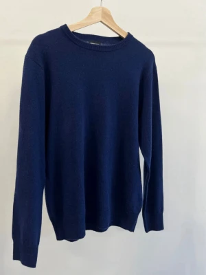 Mörkblå Kashmir/merinoull tröja - En enkel och stilren mörkblå stickad tröja med rund halsringning och långa ärmar. Tröjan har ribbade muddar vid ärmslut och nederkant, vilket ger en snygg passform. Perfekt att matcha med jeans för en clean look. Tröjan är helt ny och aldrig använd. Kostar 800kr ny. Tröjan är i kashmir och merinoull blend i riktig bra kvalitet om du har någon fråga är det bara att höra av sig mvh Levi.