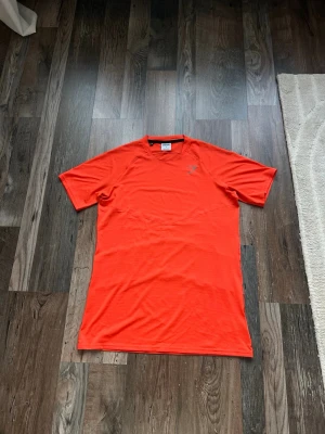 Orange tränings-tshirt från gymshark  - Snygg orange tränings-tshirt från gymshark. Tillverkad i ett lätt och snabbtorkande funktionsmaterial som passar perfekt för löpning eller gym. Med loga på bröstet och ventilerande meshdetaljer på ryggen.