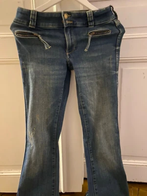 Bootcut leg adjustable waist low waist  - Säljer ett par blå bootcut jeans med slitningar och två dragkedjefickor framtill. Jeansen har normal midja, bälteshällor och klassisk knappgylf. Materialet är denim i bomull med en snygg tvättad look.