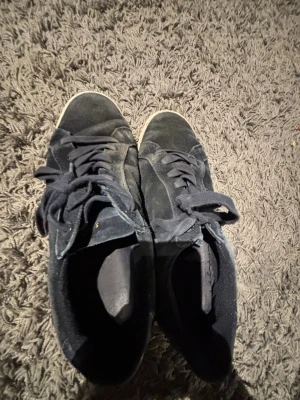 Svarta låga sneakers i mocka - Snygga svarta sneakers i mocka med klassisk låg profil och svarta skosnören. Yttersulan är vit vilket ger en schysst kontrast till resten av skon. Perfekta för dig som gillar en clean och enkel stil.