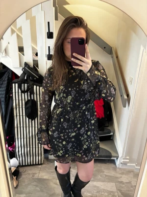 Svart blommig klänning - Snygg svart klänning med blommigt mönster och transparenta långärmar. Klänningen har volangdetaljer vid ärmslut och hals, samt markerad midja. Perfekt för dig som gillar en romantisk och trendig stil. Pris kan diskuteras💖