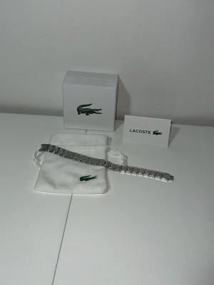 Silverfärgat armband från Lacoste - Snyggt armband i silverfärgad metall från Lacoste. Armbandet har en stilren och modern design med länkstruktur och kommer med originalpåse och ask med Lacoste-logga. Perfekt accessoar för dig som gillar klassisk men trendig stil.