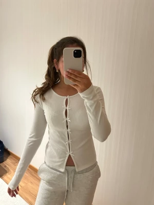 Vit långärmad topp med rosetter - Vit långärmad topp med rosetter framtill. Toppen är ribbad och har en tight passform. Knappt använd