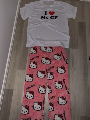 Hello Kitty pyjamas  - Säljer ett gulligt pyjamas-set med en vit t-shirt med texten 'I ❤️ My GF' och ett par rosa byxor med Hello Kitty-motiv. Byxorna är mjuka och har ett fluffigt material, perfekta för mysiga kvällar. Perfekt för dig som älskar söta och lekfulla plagg.