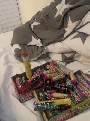 Blandade fyrverkeripjäser och smällare - Säljer ett gäng blandade fyrverkeripjäser och smällare i olika färger och former. Innehåller både mindre smällare och större pjäser, flera med färgglada etiketter och olika märken. Perfekt för dig som vill ha ett varierat utbud till nyår eller fest.