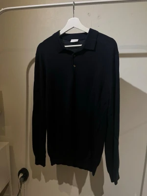 Mörkblå stickad pikétröja John Henric - Snygg mörkblå stickad pikétröja från John Henric med klassisk krage och knäppning framtill. Tröjan har långa ärmar och är tillverkad i ett mjukt, tunt material som passar perfekt till lager på lager. Enkel och stilren design som funkar till det mesta.