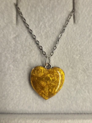 Halsband med gult hjärthänge - Snyggt halsband med ett hjärtformat hänge i skimrande gult. Kedjan är i rostfritt stål och hänget har en glansig yta som fångar ljuset. Perfekt accessoar för att addera lite färg till din outfit.