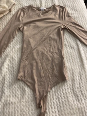 Beige långärmad body från Amisu - Säljer en beige body från Amisu i storlek XXS. Bodyn har långa ärmar, rund halsringning och är tillverkad i ett mjukt, stretchigt material. Perfekt att styla med jeans eller kjol för en clean och enkel look.