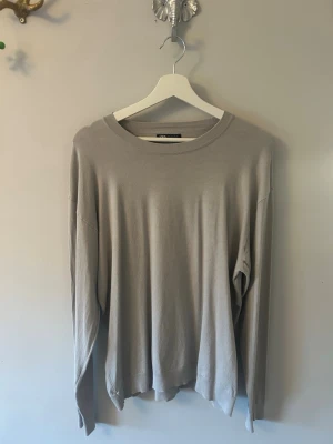 Beige långärmad tröja Zara - En stilren beige långärmad tröja från Zara med rund halsringning. Tröjan har en avslappnad passform och är tillverkad i ett mjukt, tunt material som passar perfekt för lager på lager. Enkel och clean design utan tryck eller mönster.