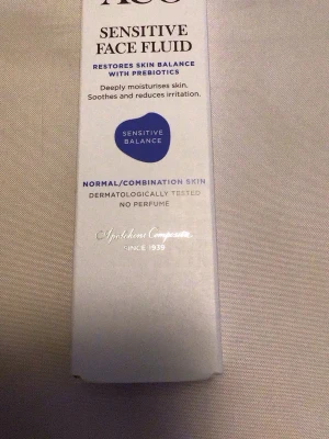 ACO Sensitive Face Fluid foundation - ACO Sensitive Face Fluid är en foundation för normal/kombinerad hud. Den är parfymfri, dermatologiskt testad och innehåller prebiotika, hyaluronsyra och panthenol som återfuktar och lugnar huden. Produkten kommer i en vit förpackning och innehåller 50 ml.