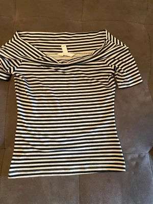 Randig off sopshoulder topp H&M XS - Säljer en svartvit, figurnära topp från H&M i storlek XS. Toppen har off shoulder-modell och smala horisontella ränder. Materialet är mjukt och stretchigt, perfekt för en trendig och avslappnad look.