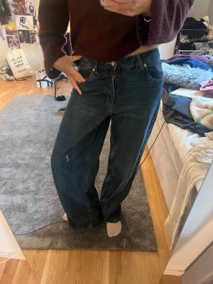 blåa baggy  jeans - Säljer ett par mörkblåa jeans med bred passform och hög midja. Jeansen har klassiska fem fickor och raka, vida ben. Materialet är kraftig denim i bomull. Perfekta för en avslappnad och trendig look.