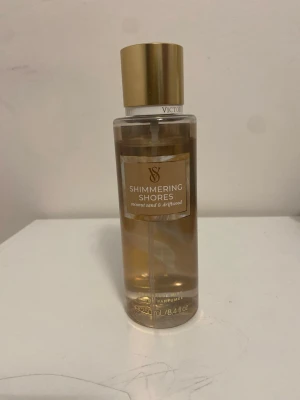 Victoria's Secret Shimmering Shores parfym - Fräsch parfym från Victoria's Secret i doften Shimmering Shores med inslag av kokos, sandelträ och vaniljorkidé. Flaskan är genomskinlig med guldigt lock och rymmer 250 ml. Perfekt för dig som gillar tropiska och varma doftnoter.