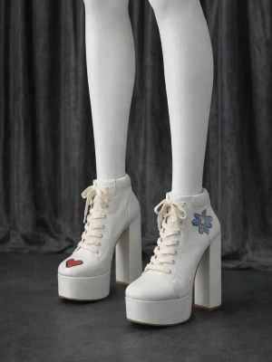 Vita platåpumps med broderi - Unika vita platåpumps med kraftig klack och snörning framtill. Skorna har handmålade detaljer: ett rött hjärta på tån och en blå blomma på sidan. Tillverkade i konstläder med chunky retrostil som sticker ut.