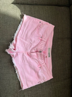 Rosa jeansshorts  - Säljer ett par ljusrosa jeansshorts från Moto med råa, fransiga kanter och klassisk femficksdesign. Shortsen har knapp och dragkedja framtill samt bälteshällor. Perfekta för varma dagar och ger en avslappnad vibe. 