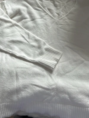 Vit stickad v-ringad tröja - Vit stickad tröja med v-ringning och långa ärmar. Tröjan har ribbade muddar vid ärmslut och nederkant, vilket ger en snygg och klassisk look. Perfekt att styla med jeans eller kjol.