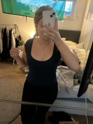 Mörkblå tight topp med djup urringning - Snygg mörkblå topp med tight passform och djup, rund urringning. Korta ärmar och stretchigt material som sitter skönt mot kroppen. Perfekt att styla med jeans eller kjol för en trendig look.