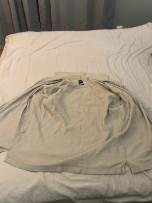 Ljusbeige kortärmad skjorta - Säljer en ljusbeige kortärmad skjorta med klassisk krage och bröstficka. Skjortan har knäppning framtill och är tillverkad i ett tunt, mjukt tyg som passar perfekt till sommaren. Enkel och stilren design som funkar till många olika outfits.