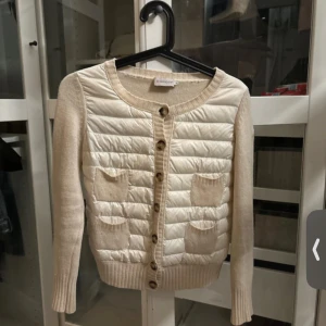  Moncler cardigan  - Supersnygg beige kofta från Moncler med quiltad framsida och stickade ärmar. Rund halsringning, knappar framtill och två små fickor. Perfekt för lager-på-lager och ger en lyxig vibe till din outfit. OBS!! Krympt i tvätten så egentligen storlek S men nu XXS, små smink fläckar som man kan se på bilden går säkert bort på kemtvätt. 