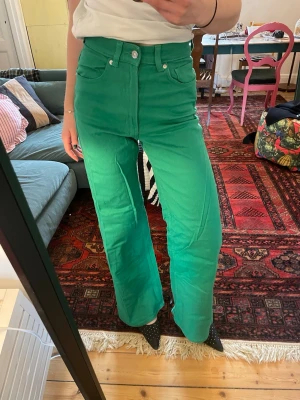 Gröna raka jeans med hög midja - Säljer ett par coola gröna jeans med hög midja och raka ben. Jeansen har klassiska fem fickor och silverfärgade knappar. Materialet är denim och färgen är riktigt grön, perfekt för dig som vill sticka ut. Passar dig som gillar trendiga och färgstarka plagg.