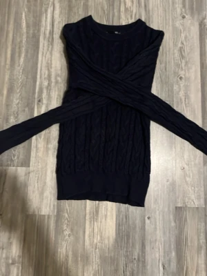 Mörkblå kabelstickad tröja - Snygg mörkblå kabelstickad tröja med rund halsringning och ribbade muddar vid ärmslut och nederkant. Tröjan har ett klassiskt flätmönster och är perfekt för dig som gillar en stilren och mysig look. Materialet känns mjukt och bekvämt.