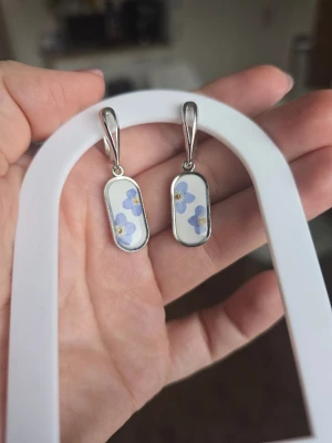 Örhängen med förgätmigej - Unika örhängen i silverfärg med förgätmifej inuti på vit bakgrund. De har en modern och stilren design med blommor som ger en söt och personlig touch. Perfekta för dig som gillar detaljer och vill sticka ut.