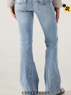 Ljusblå bootcut jeans True Religion - Säljer ett par ljusblå bootcut jeans från True Religion med ikoniska fickdetaljer och kontrastsömmar. Jeansen har låg midja och klassisk femficksdesign. Tillverkade i mjuk denim med stretch för skön passform. Något slitna vid hälen