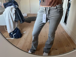 Gråa jeans med fickor från Gina tricot  - Säljer ett par gråa jeans från Gina tricot med bootcut passform och snygga fickor med lock och knapp bak. Jeansen har klassisk femficksdesign och är tillverkade i mjukt denim-material. Perfekt för dig som vill ha en cool och avslappnad look.💕