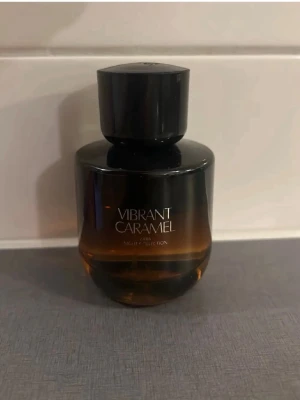 Vibrant Caramel parfym från Zara - En elegant parfymflaska från Zara med namnet Vibrant Caramel. Flaskan är rund och har en gradient färg från mörkbrun till karamellton, med svart lock. Perfekt för dig som gillar söta och varma dofter.70%kvar