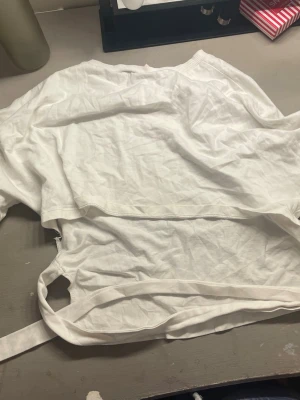 Vit croppad omlottopp med knytband - Säljer en vit croppad omlottopp med knytband i midjan. Toppen är ärmlös och har en enkel, clean design som passar perfekt till jeans eller kjol. Tillverkad i mjuk bomull för en skön känsla. Perfekt för dig som gillar minimalistisk stil.