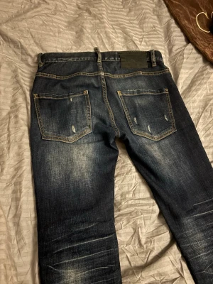 Mörkblå Dsquared2 jeans herr - Säljer ett par mörkblå Dsquared2 jeans i storlek 44. Jeansen har slitna detaljer, raka ben och klassiska bakfickor. Tillverkade i Italien med snygg tvätt och kontrastsömmar. Perfekta för dig som gillar streetwear och exklusiva märken. Priset är diskuterbart 
