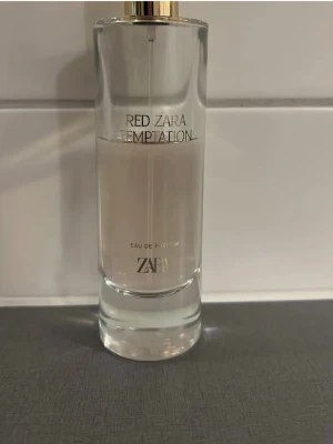 Zara Red Temptation Eau de Parfum - Zara Red Temptation Eau de Parfum i en elegant, genomskinlig glasflaska med gulddetaljer. Doften är modern och flaskan har en stilren, cylindrisk form med enkel text i svart. Perfekt för dig som gillar trendiga och fräscha parfymer.
