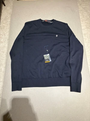 Mörkblå tröja från Morris - Stilren mörkblå tröja från Morris med rund halsringning och diskret logga broderad på bröstet. Tröjan har ribbade muddar vid ärmslut och nederkant. Tillverkad i mjukt material som passar perfekt till lager-på-lager. NYPRIS 1599kr