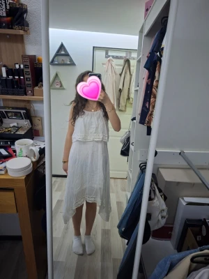 Vit omlottklänning med spetsdetaljer - Säljer en luftig vit klänning med omlottkänsla och spetsdetaljer. Klänningen har asymmetrisk längd, volang upptill och tunna axelband. Perfekt för sommarens varma dagar och ger en romantisk vibe.